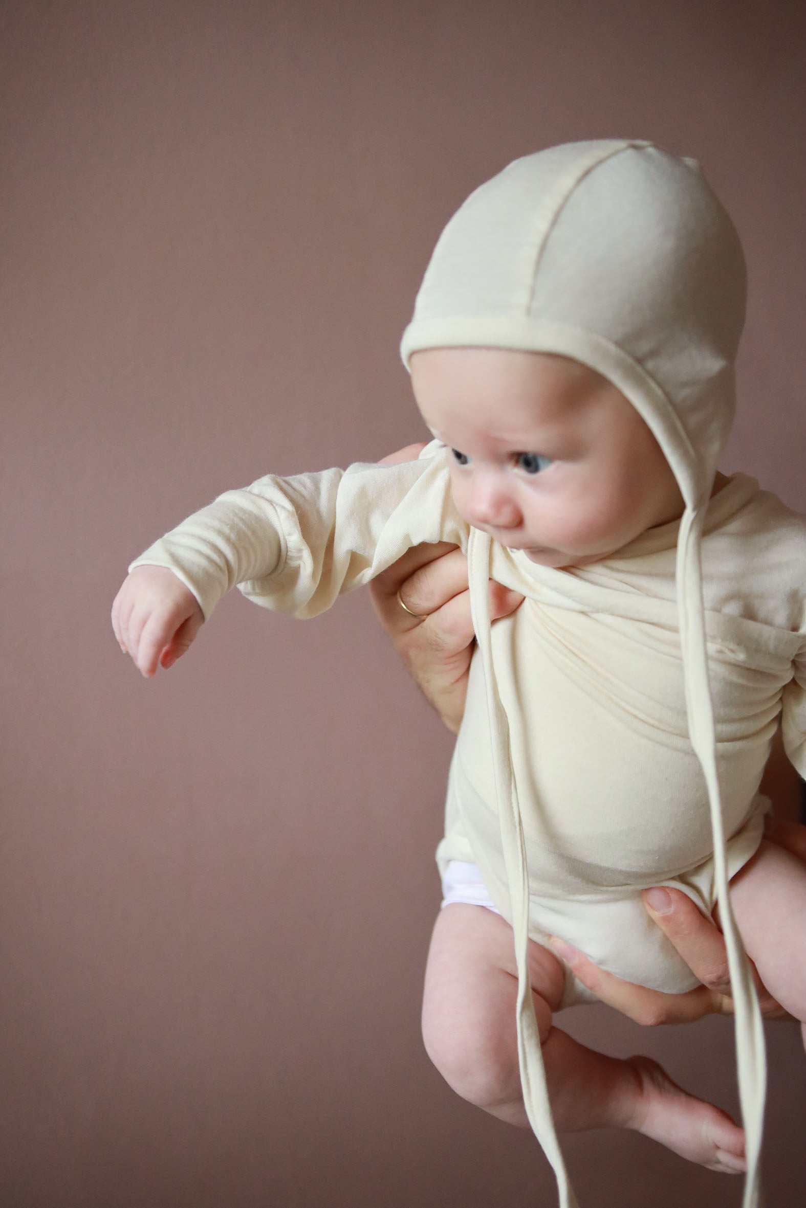 Ein Baby trägt den Loopbody Seide-Viskose – Natur, einen knopf- und nahtlosen Langarmbody, der sich dem Körper anpasst und einfaches Anziehen ermöglicht. Baby Body für Erstausstattung Baby.