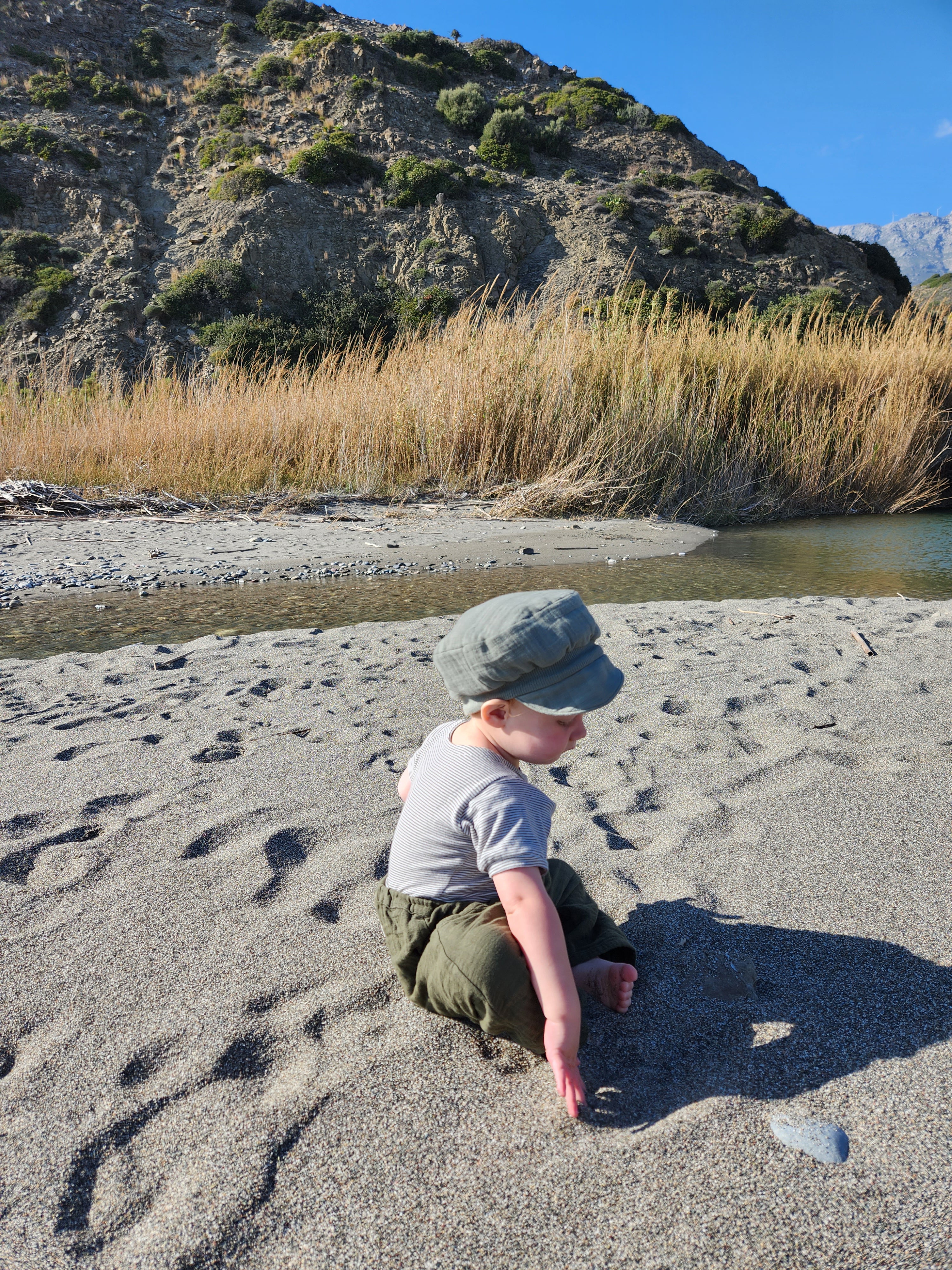 Kleinkind am Strand trägt die Michelmütze Bio-Musselin - Taube, eine luftige Sommermütze aus Bio-Baumwolle, schützt effektiv vor Sonne.